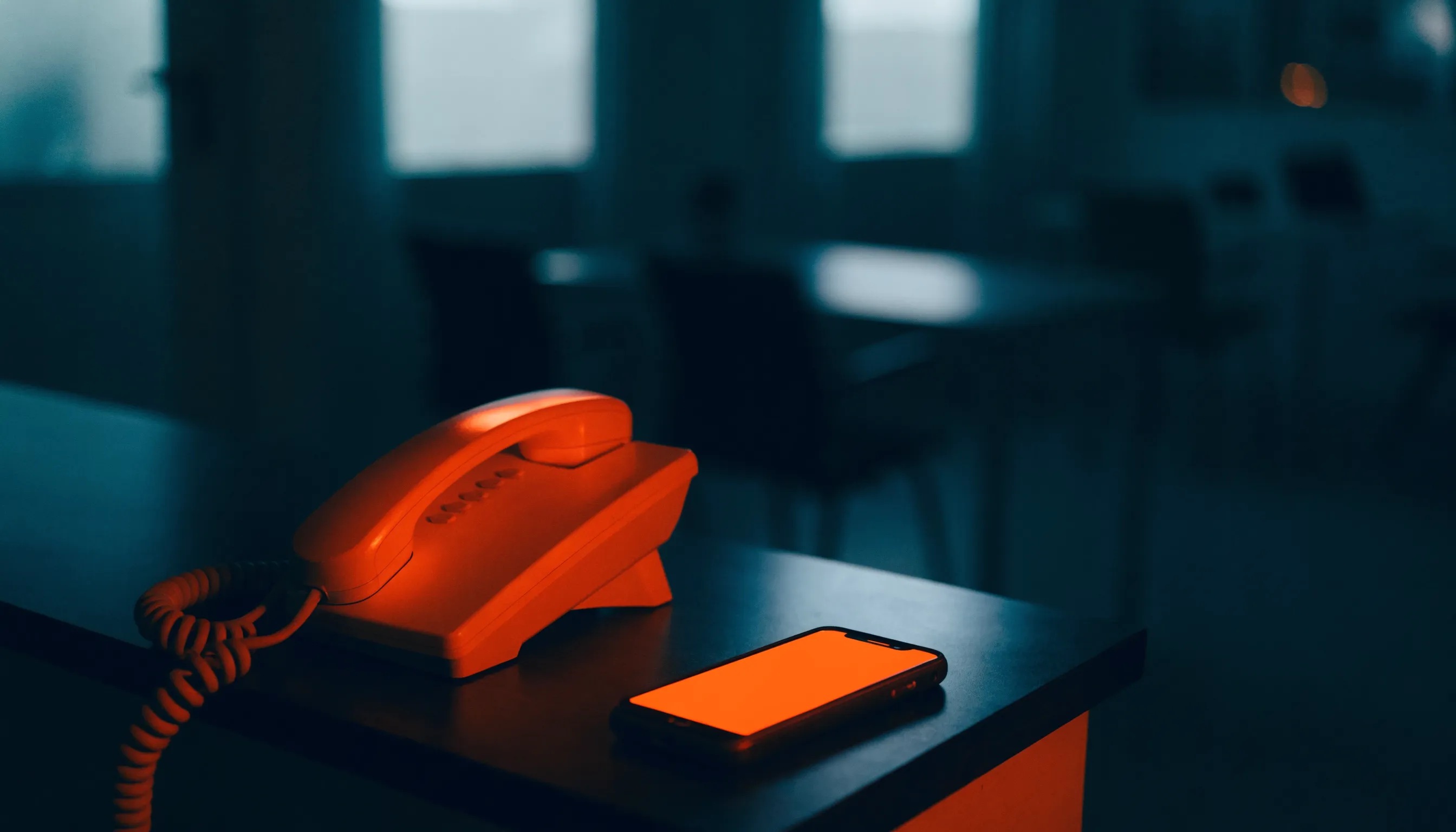 A dark reception desk at night with a phone glowing orange, answering on its own