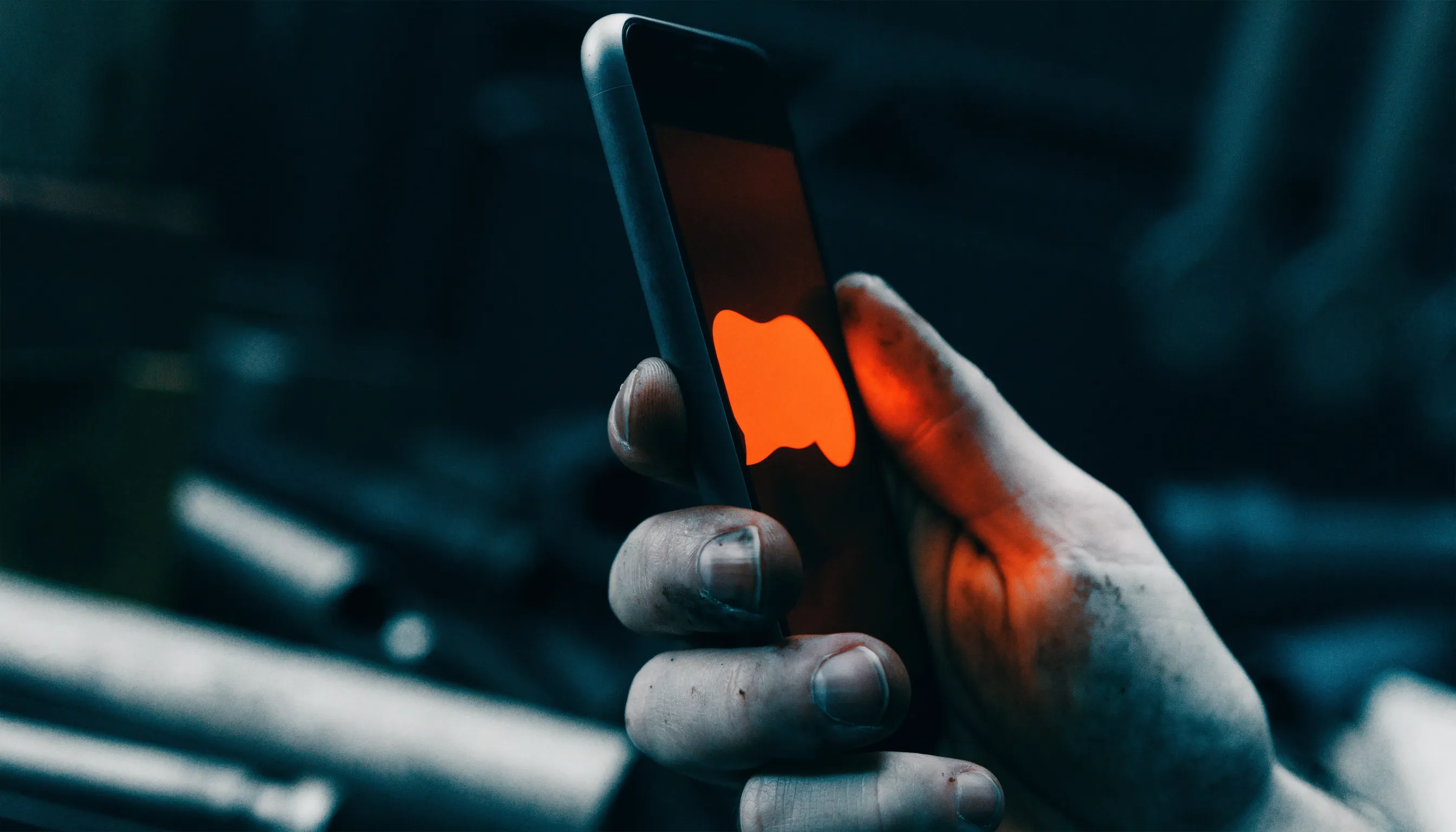 A tradesperson's work-worn hand holding a phone glowing orange with a text message