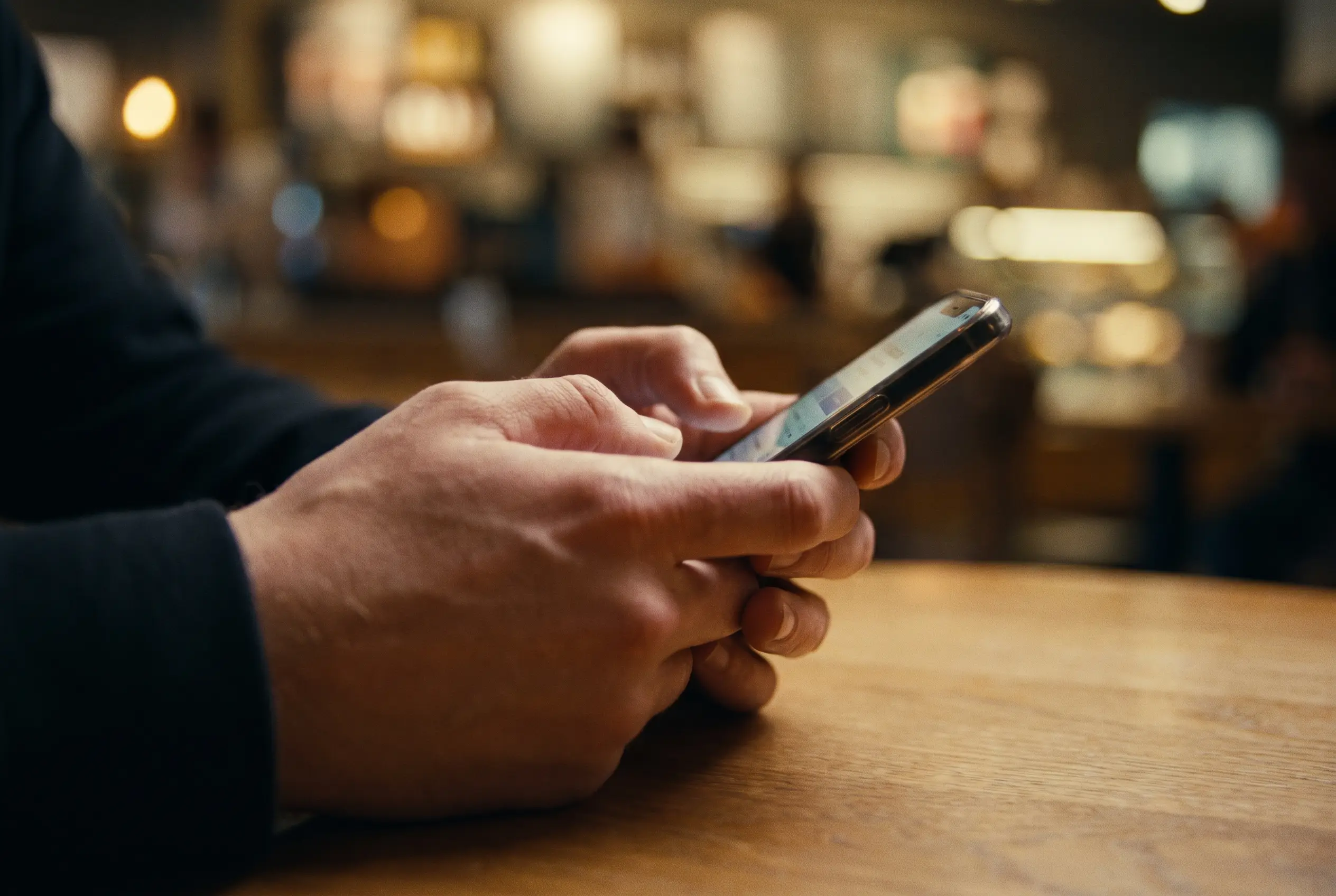Hands holding a phone in a dim cafe, screen glow on the fingers