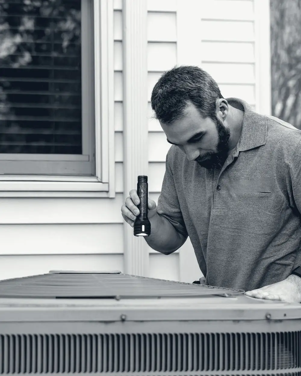 Technician inspecting an outdoor air conditioning unit with a flashlight