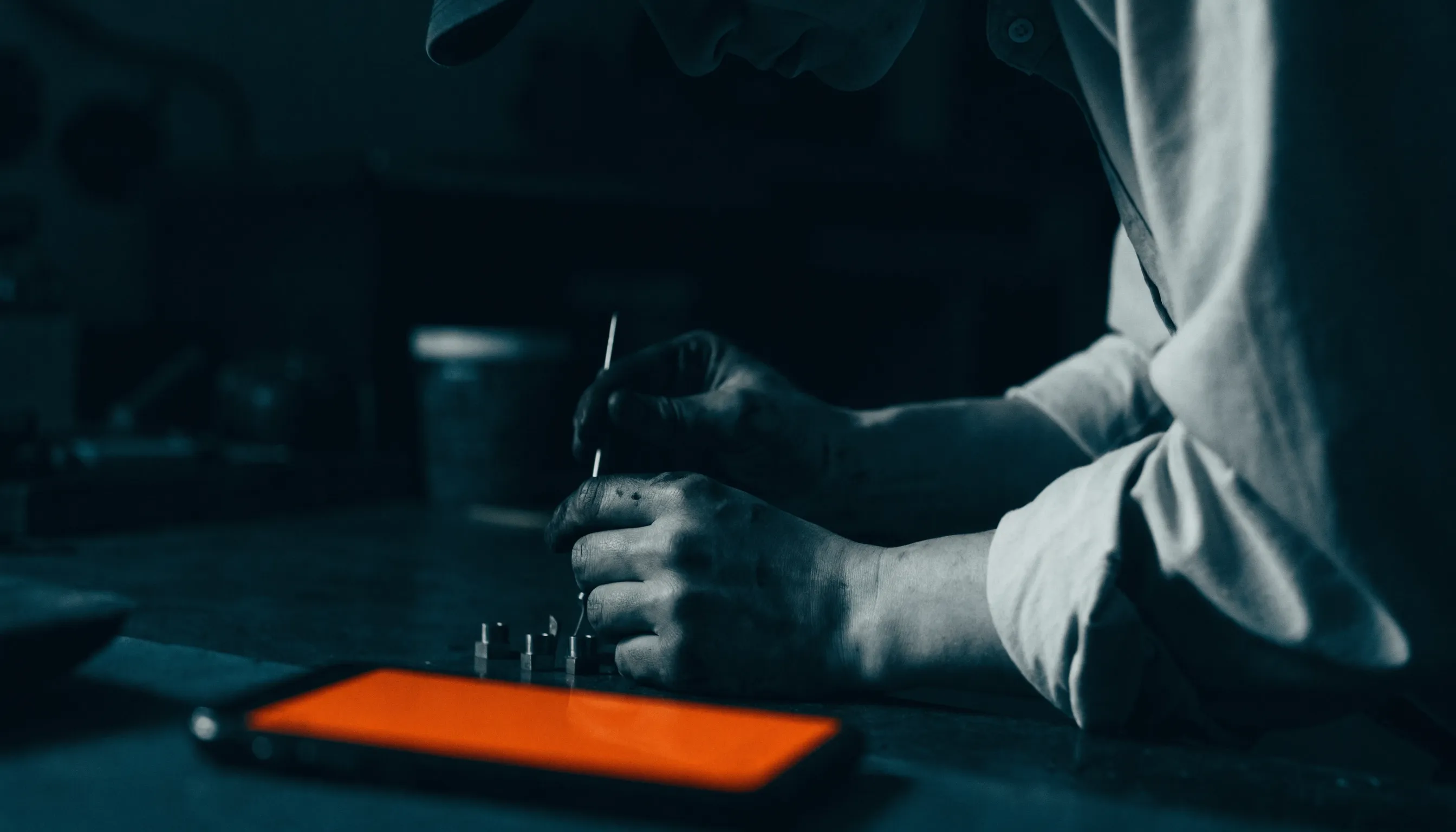 A tradesperson working in a dim workshop with a smartphone glowing orange with a missed call on the bench